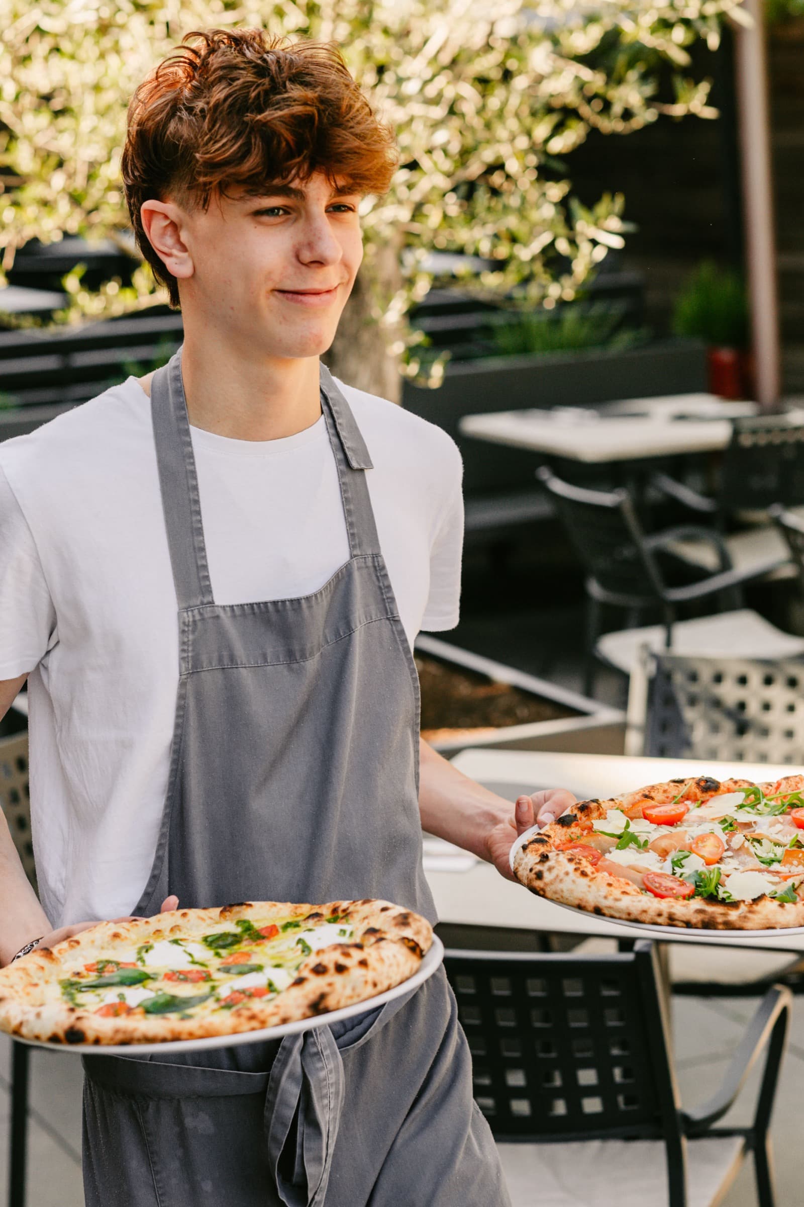 Mitarbeiter trägt zwei Pizzen auf der Terrasse